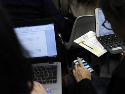 Duas pessoas trabalham com seus computadores e celulares, em uma imagem de arquivo.