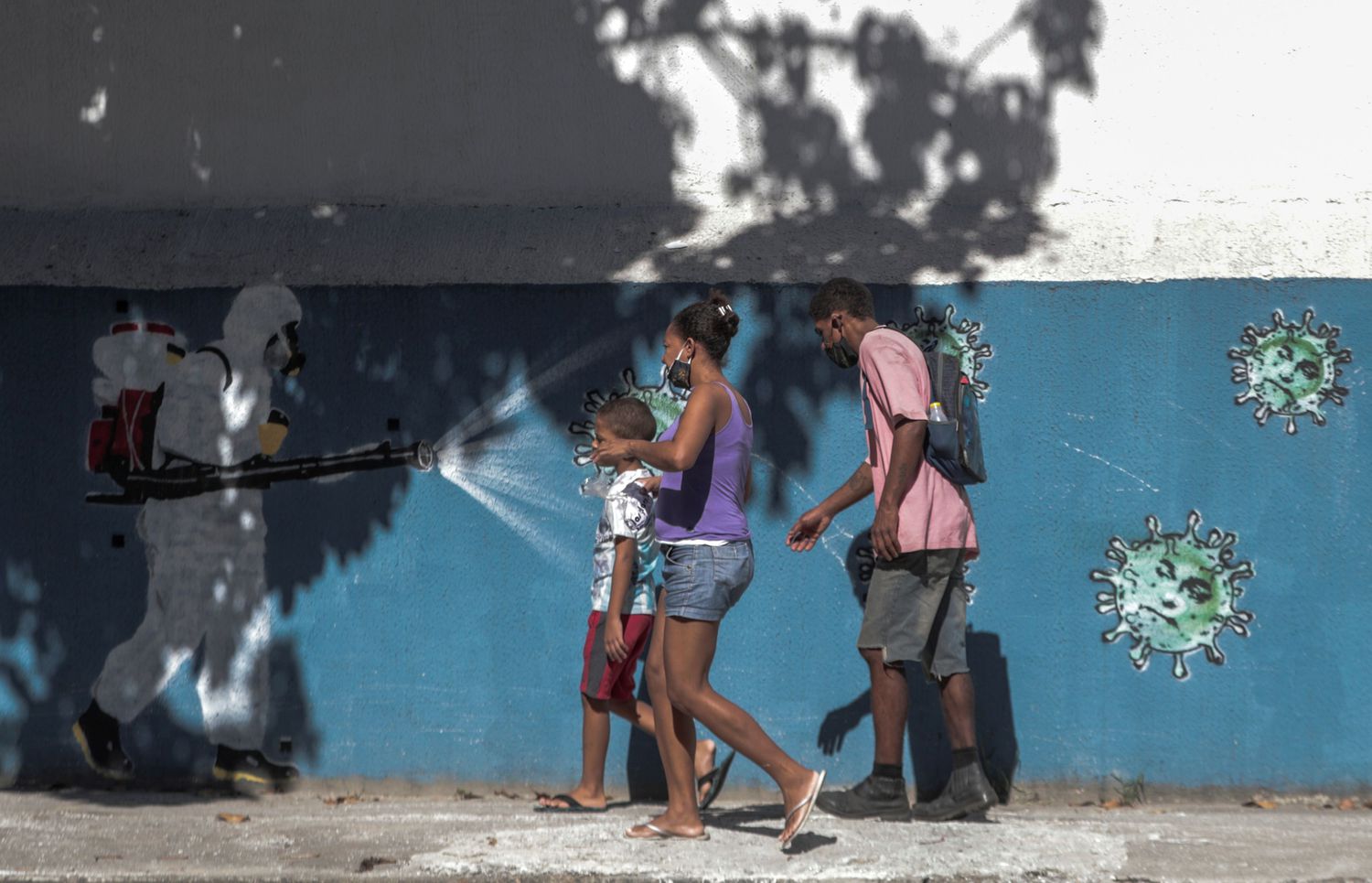 Família passa por um grafite que mostra profissional da saúde pulverizando coronavírus no rosto do presidente Jair Bolsonaro, no dia 22 de junho.