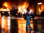 A person holding a phone walks past burning vehicles following demonstrations protesting the death of George Floyd, a black man who died May 25 in the custody of Minneapolis Police, in Seattle, Washington on May 30, 2020. - Demonstrations are being held across the US after George Floyd died in police custody on May 25. (Photo by Jason Redmond / AFP)