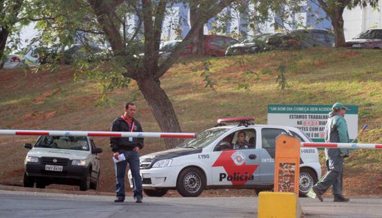 Policial e funcionários na frente da fábrica assaltada, em Campinas.