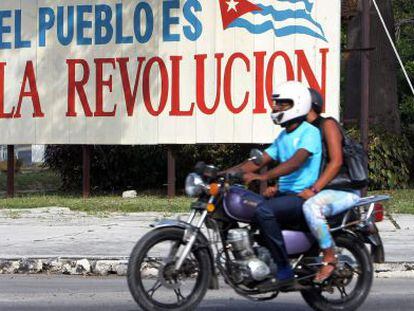 Motociclistas passam por cartaz alusivo à revolução cubana, em Havana.