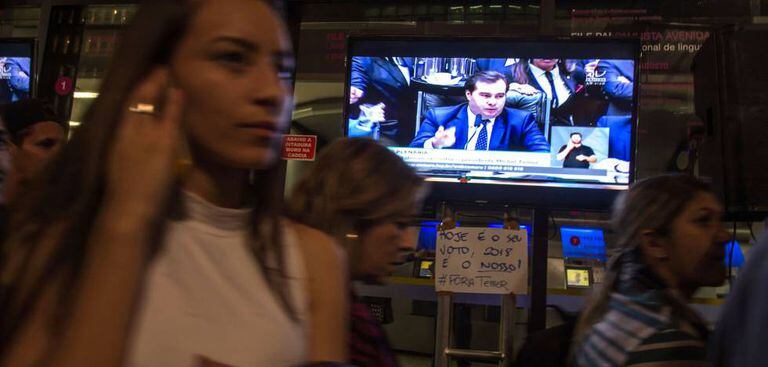 Pessoas passam diante de TV durante votação na Câmara, nesta quarta.