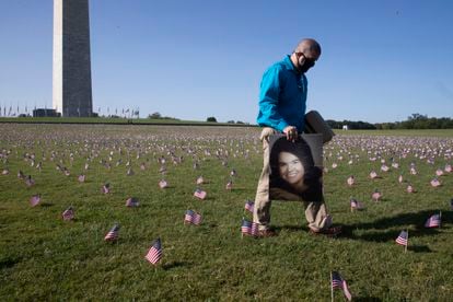 Um homem passa com um retrato de sua mãe, que morreu de covid-19, entre as milhares de bandeiras colocadas ao lado da base do obelisco de Washington em homenagem às vítimas do novo coronavírus, no dia 22 de setembro.