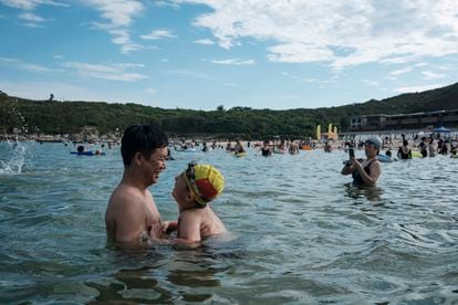 Uma criança com uma touca de natação com a bandeira da China é vista com o pai, na praia de Dongchong.