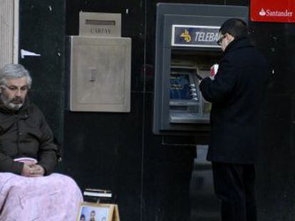 Um homem pede esmolas na porta de um caixa automático em Madri.