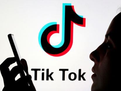 Uma pessoa segura um celular em frente ao logotipo da rede social chinesa TikTok.