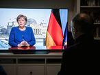 People watch as German Chancellor Angela Merkel delivers her first direct TV address to the nation in over 14 years in power, in a living room, in Oberhausen, Germany, Wednesday, March 18, 2020. For most people, the new coronavirus causes only mild or moderate symptoms, such as fever and cough. For some, especially older adults and people with existing health problems, it can cause more severe illness, including pneumonia. (Fabian Strauch/dpa via AP)