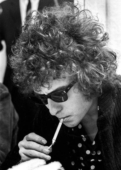 Dylan durante uma coletiva de imprensa na Suécia (1966). Convertido ao rock, e como membro da Geração Beat, sua imagem muda deixando crescer o cabelo – que, cacheado e revolto, lhe dá um ar sexy; utiliza os Way Farer, da Ray Ban, e começa a se vestir de preto, com camisas estampadas que o caracterizam como ícone roqueiro. Menção especial ao comprimento das unhas da mão direita com a qual acende o cigarro.