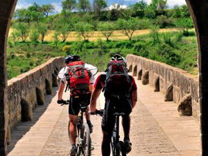 Dois ciclistas na ponte românica de Puente la Reina, na passagem do Caminho de Santiago por Navarra.