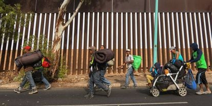 Migrantes centro-americanos caminham nesta terça-feira em Mexicali (México) ao lado da cerca na fronteira com os EUA.