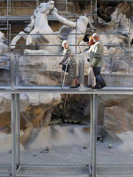 Três visitantes passeiam pela passarela sobre a Fontana de Trevi.