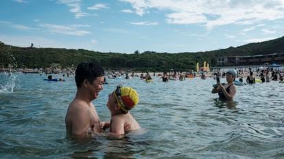Uma criança com uma touca de natação com a bandeira da China é vista com o pai, na praia de Dongchong.