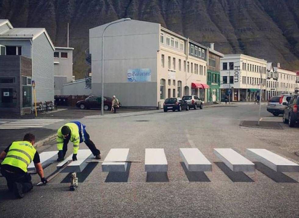 Dois operários pintam a faixa tridimensional em Ísafjörður (Islândia).