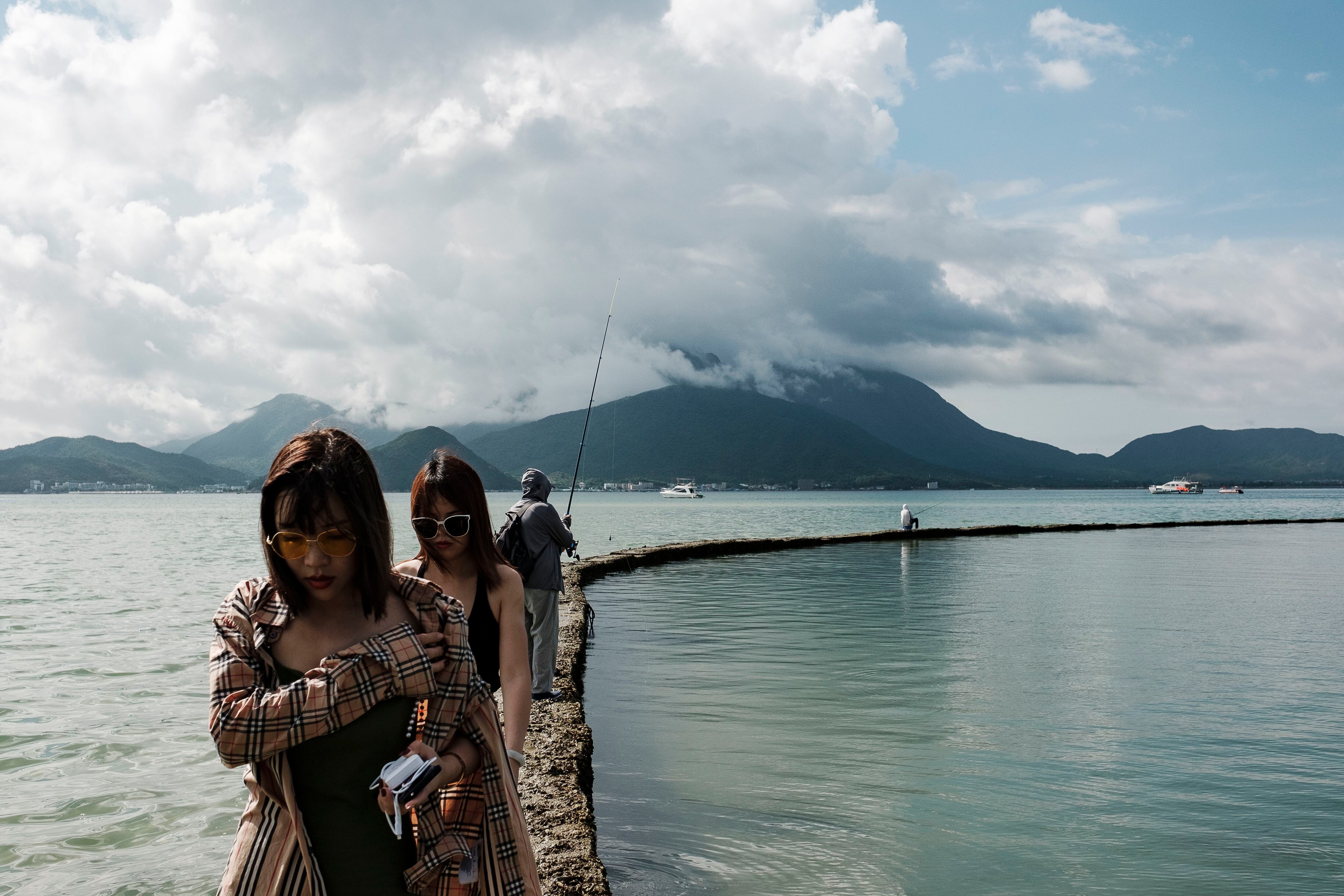 Turistas chinesas são vistas caminhando em um muro artificial, na praia de Dapeng Jiaochangwei.
