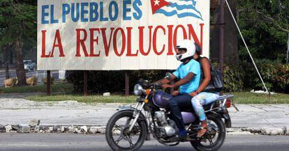 Motociclistas passam por cartaz alusivo à revolução cubana, em Havana.