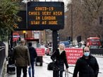 Pedestrians, some wearing a face mask or covering due to the COVID-19 pandemic, walk past a sign alerting people that "COVIDCOVID LONDON-19 cases are very high in London - Stay at Home", in central London on December 23, 2020. - Britain's public health service urged Prime Minister Boris Johnson on Wednesday to extend the country's Brexit transition period or risk pushing hospitals already struggling with coronavirus "over the edge" in the event of a no-deal departure from the EU single market. (Photo by Tolga Akmen / AFP)
