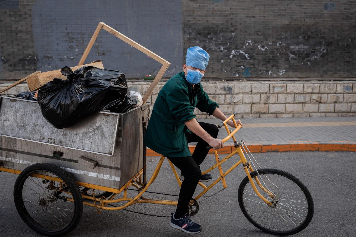 Trabalhador usando uma máscara leva carregamento de lixo em seu triciclo.