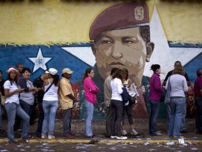 Fila em Caracas diante de um muro pintado com o rosto de Hugo Chávez.