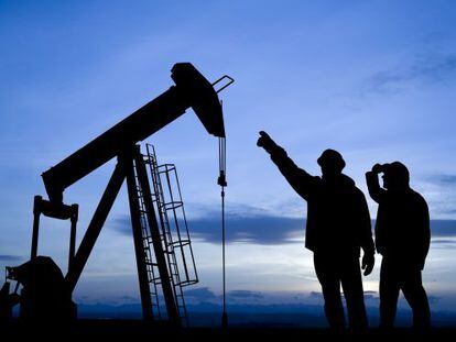 Dois trabalhadores observam um poço de extração de petróleo
