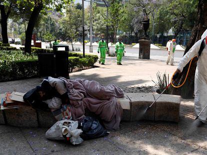 Agentes sanitários lavam praça no México, enquanto morador de rua dorme, em uma imagem de abril do ano passado.