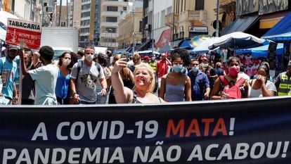 Uma mulher sem máscara, no centro de São Paulo, tira uma selfie atrás de uma faixa que diz: "A Covid-19 mata. A Pandemia não acabou".