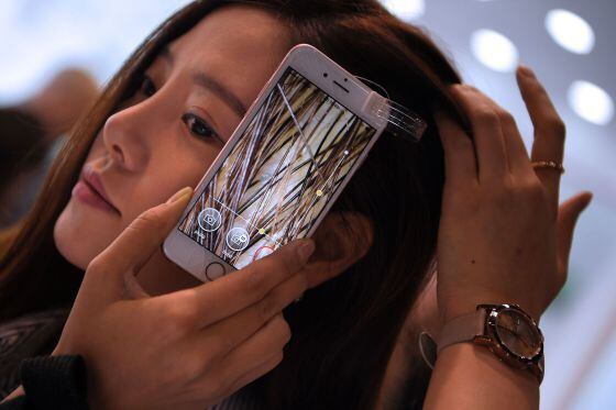 Uma mulher prova a microcâmera de um celular que permite ver o interior de seu cabelo.