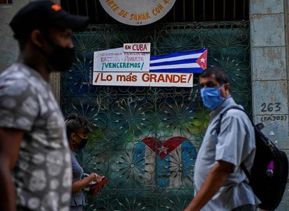 Varias personas caminan frente a una bandera de Cuba, en La Habana