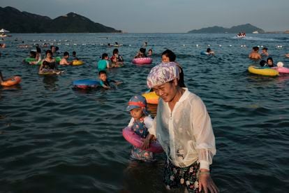 Uma mulher com uma touca de banho leva uma criança em meio a banhistas na praia de Xichong. 