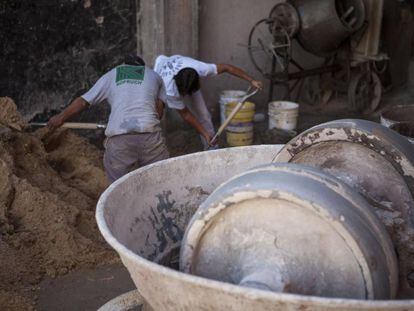 Operários da construção civil preparam mistura de areia e cimento.