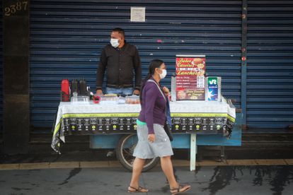 Uma mulher passa por um vendedor ambulante no centro de São Paulo, ambos usando máscara de proteção, nesta segunda-feira.