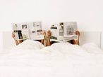 Una pareja en la cama leyendo periódicos.