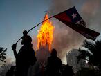 TOPSHOT - A demonstrator flutters a Chilean flag outside the burning church of Asuncion, set on fire by protesters, on the commemoration of the first anniversary of the social uprising in Chile, in Santiago, on October 18, 2020, as the country prepares for a landmark referendum. - Two churches were torched as tens of thousands of demonstrators gathered Sunday in a central Santiago square to mark the anniversary of a protest movement that broke out last year demanding greater equality in Chile. The demonstration comes just a week before Chileans vote in a referendum on whether to replace the dictatorship-era constitution -- one of the key demands when the protest movement began on October 18, 2019. (Photo by MARTIN BERNETTI / AFP)