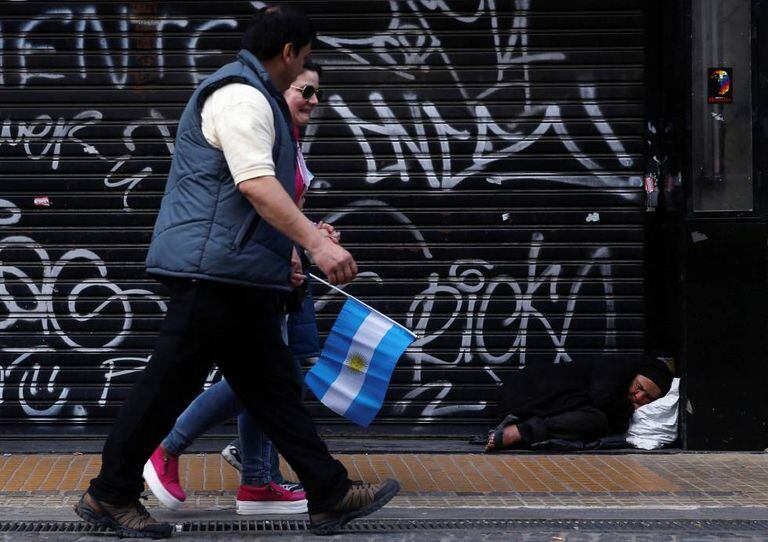 Mulher dorme na calçada enquanto pessoas caminham durante a celebração do bicentenário da independência argentina, em Buenos Aires.
