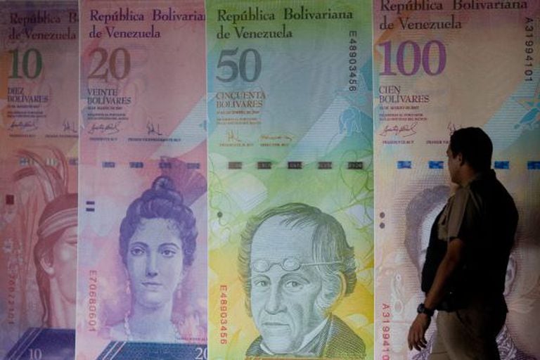 Um homem caminha em frente a cartazes de cédulas venezuelanas.