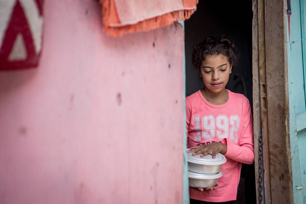 Natalia Macario, 7, recebe um prato de comida. A menina e o irmão acompanham as aulas em casa pelo celular.
