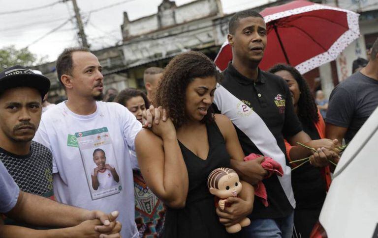 Vanessa Francisco Sales leva uma boneca que foi de sua filha, Ágatha Félix. Está de mãos dadas com Adegilson Félix, seu marido e pai da menina, durante o velório.