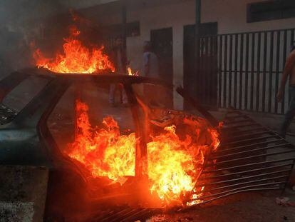 Um manifestante passa junto a um carro em lumes utilizado como barricada.
