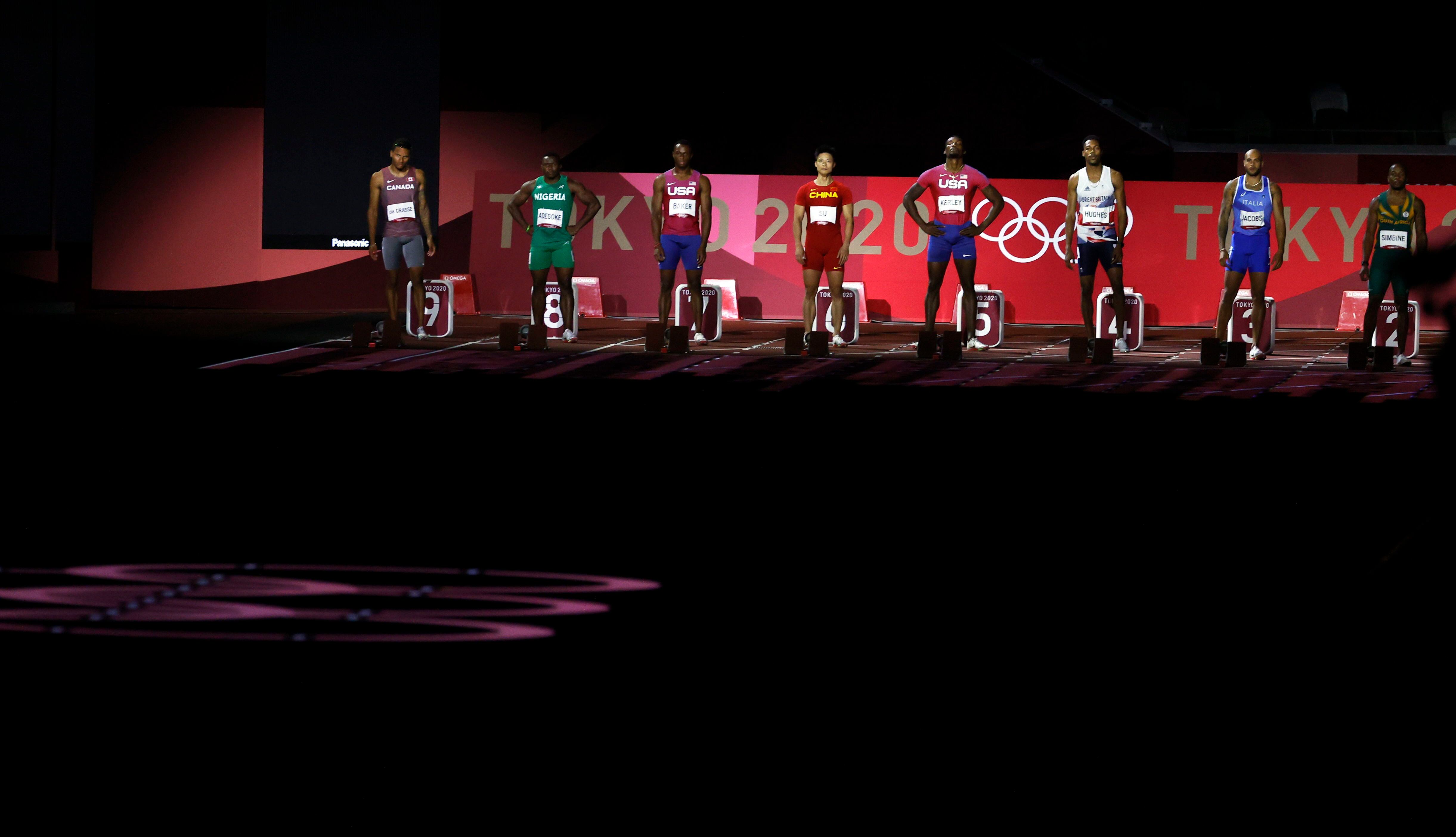 Os atletas alinhados em suas marcas antes de correr a final dos 100m no Estádio Olímpico de Tóquio.
