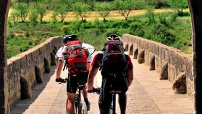 Dois ciclistas na ponte românica de Puente la Reina, na passagem do Caminho de Santiago por Navarra.