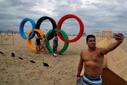 Homem faz um selfie em frente ao s&iacute;mbolo das Olimp&iacute;adas em Copacabana.
