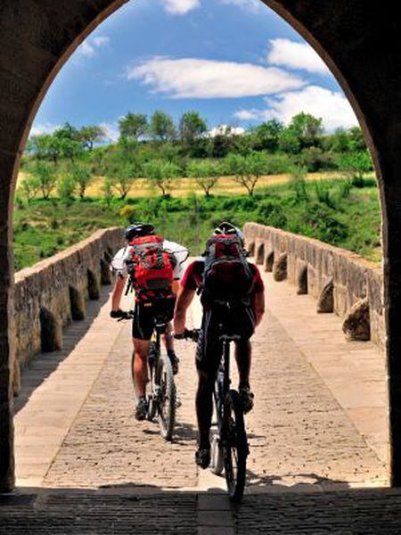 Dois ciclistas na ponte românica de Puente la Reina, na passagem do Caminho de Santiago por Navarra.