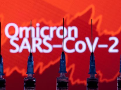 Seringas com agulhas são fotografadas em frente a um painel com gráficos e as palavras "Omicron SARS-CoV-2".