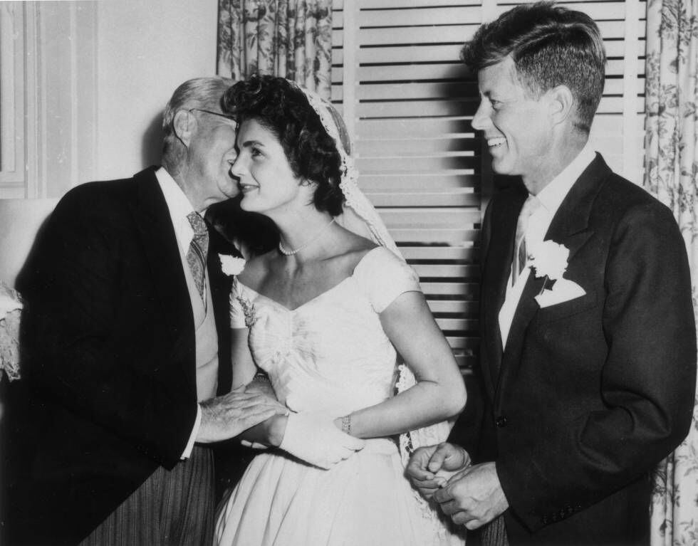 Joseph Kennedy (1888-1969) sussurra algo no ouvido de sua nova nora, Jacqueline Bouvier, no dia do casamento, enquanto o marido, John F. Kennedy, observa, sorridente. Foi em Newport, Rhode Island, em 12 de setembro de 1953. 
