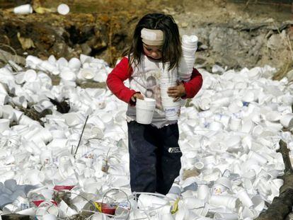 Menina recolhe copos de plástico em um lixão.