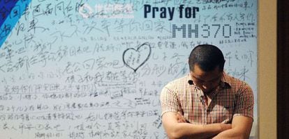 Um homem em frente a um painel com mensagens de apoio às vítimas do MH370.