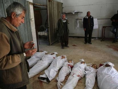 Um homem reza em frente aos cadáveres de várias crianças vítimas do último bombardeio do regime sírio.