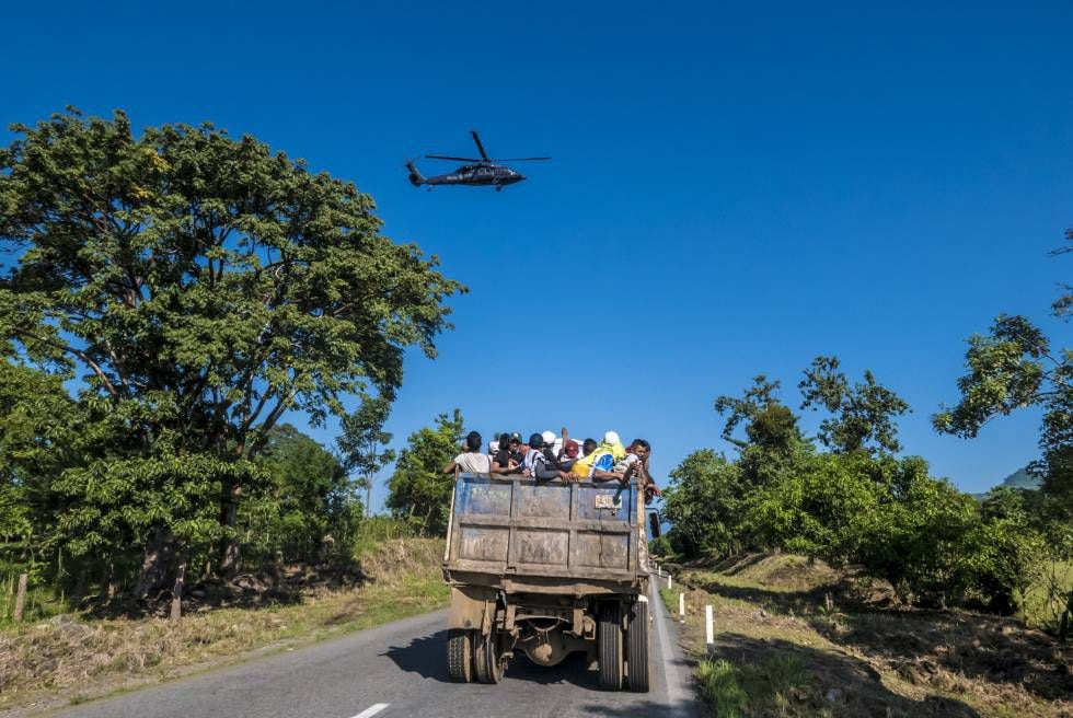 Um grupo de hondurenhos é levado em um caminhão de materiais enquanto um helicóptero da polícia federal mexicana vigia seu trajeto.