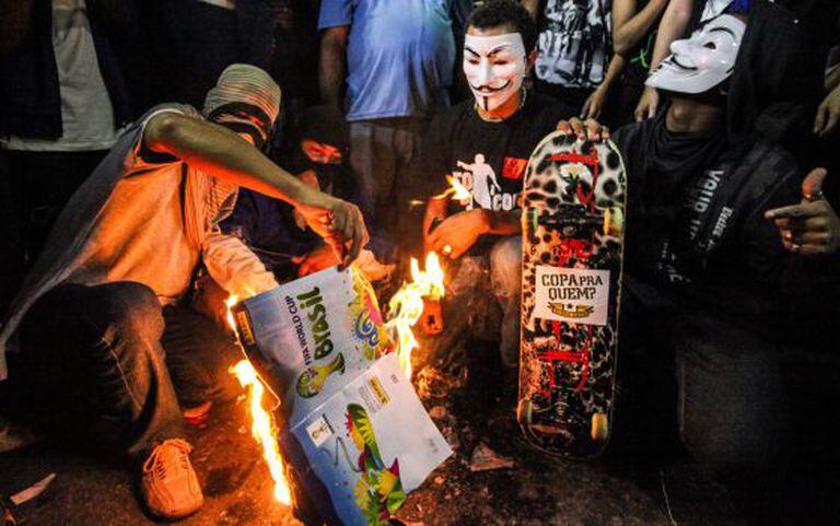 Grupo de manifestantes queima um álbum da Copa no Rio.