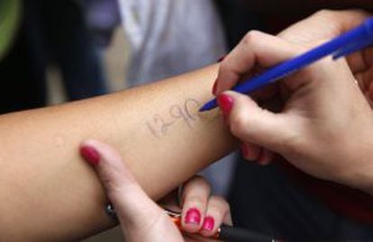 Cidadãos de San Cristóbal escrevem um número em seus braços para marcar sua vez na fila do supermercado.