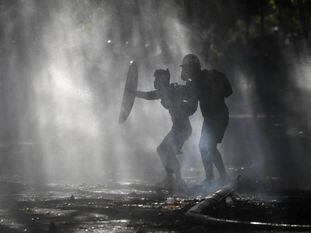 Manifestantes se defendem dos jatos d’água com os quais a polícia tenta dispersá-los, durante um protesto em Santiago.